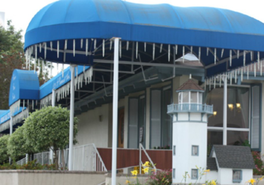 A building with a blue awning and a small lighthouse replica outside.