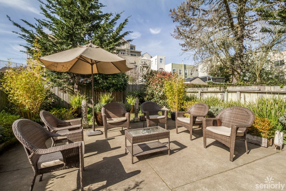 A cozy outdoor patio area with seating and an umbrella, surrounded by greenery.