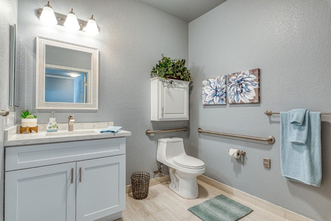 A clean and well-decorated bathroom with white cabinetry, a toilet, mirror, and wall art.