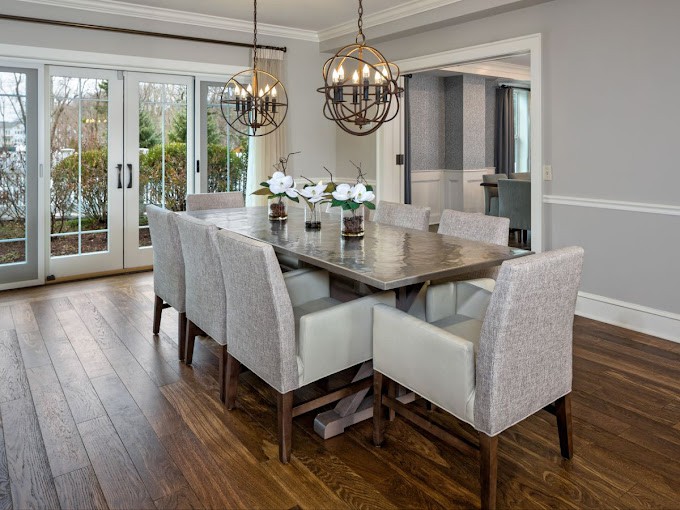 A modern dining room with elegant chandeliers, a large wooden table, and upholstered chairs.