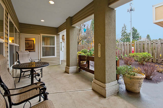 A cozy patio area with seating and plants, sheltered by a roof and supported by columns.