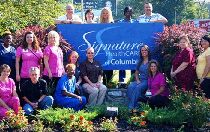 A group of healthcare staff posing with a Signature HealthCARE banner outside.
