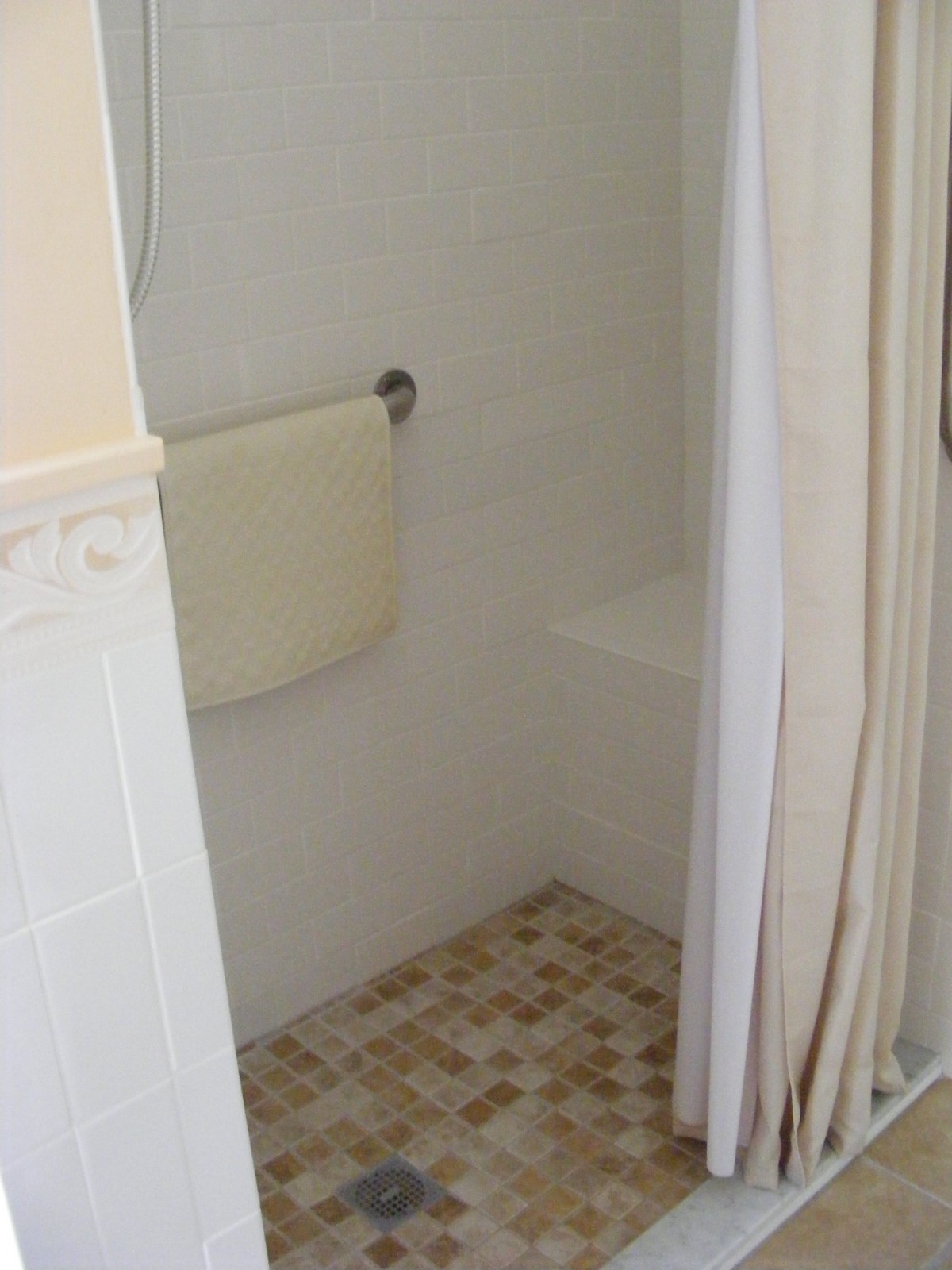 A bathroom shower area with a tile floor, curtain, and towel rack.