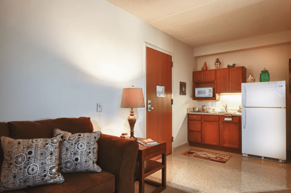 A cozy apartment interior featuring a living room area with a sofa and lamp, adjacent to a compact kitchenette.