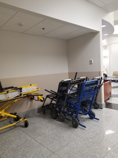 A corner of a hospital hallway featuring multiple wheelchairs and a stretcher, indicating the medical services available.
