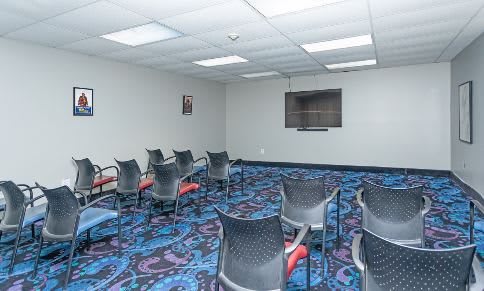 An empty meeting room with chairs arranged and a television mounted on the wall.