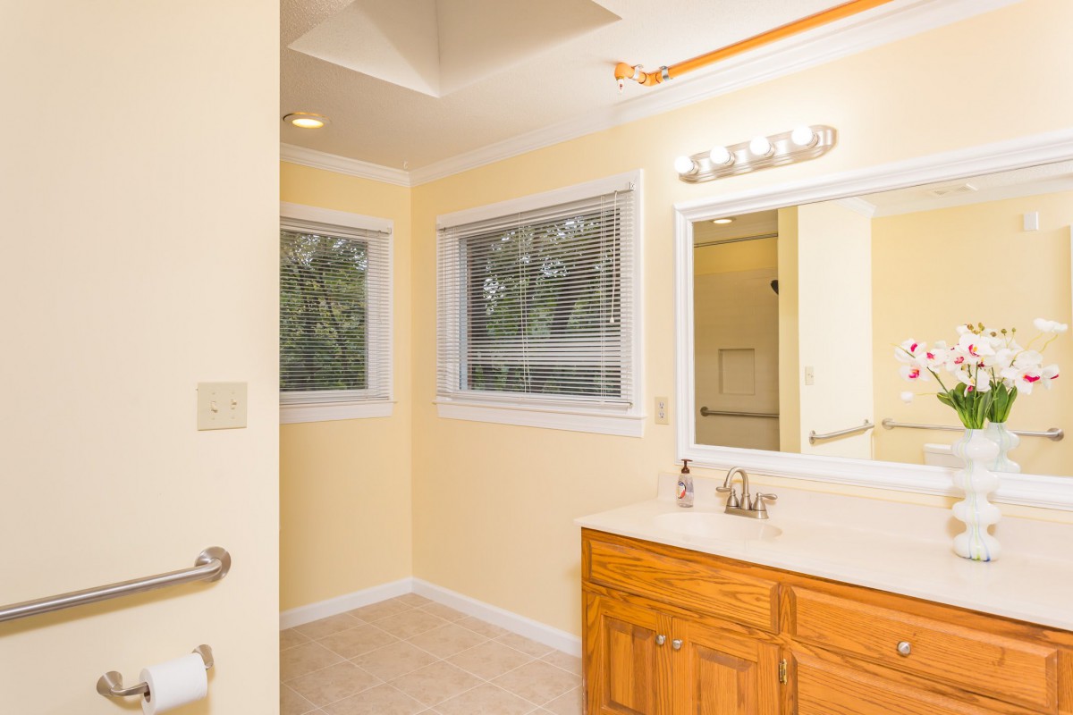 A well-lit bathroom with a wooden cabinet, large mirror, and two windows.