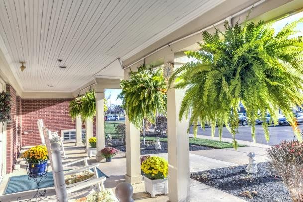 A sunny porch with hanging ferns and cozy rocking chairs invites relaxation.