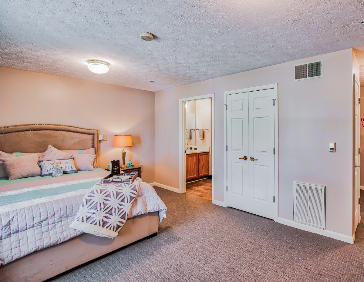 A cozy bedroom with a neatly made bed, bedside lamp, and adjoining bathroom.