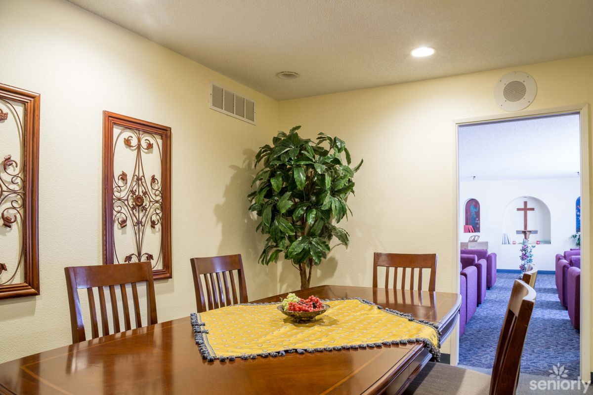 A cozy dining room with a wooden table and chairs, decorated with a centerpiece and surrounded by wall art and an indoor plant.