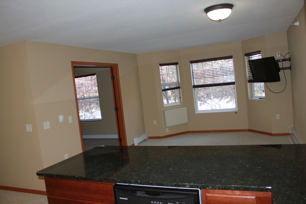 A spacious living room with large windows and a view of the kitchen counter.