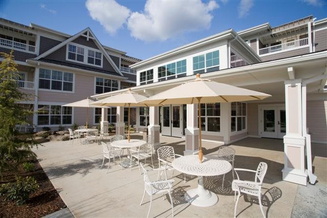 A sunny outdoor patio with tables, chairs, and umbrellas in front of a residential building.