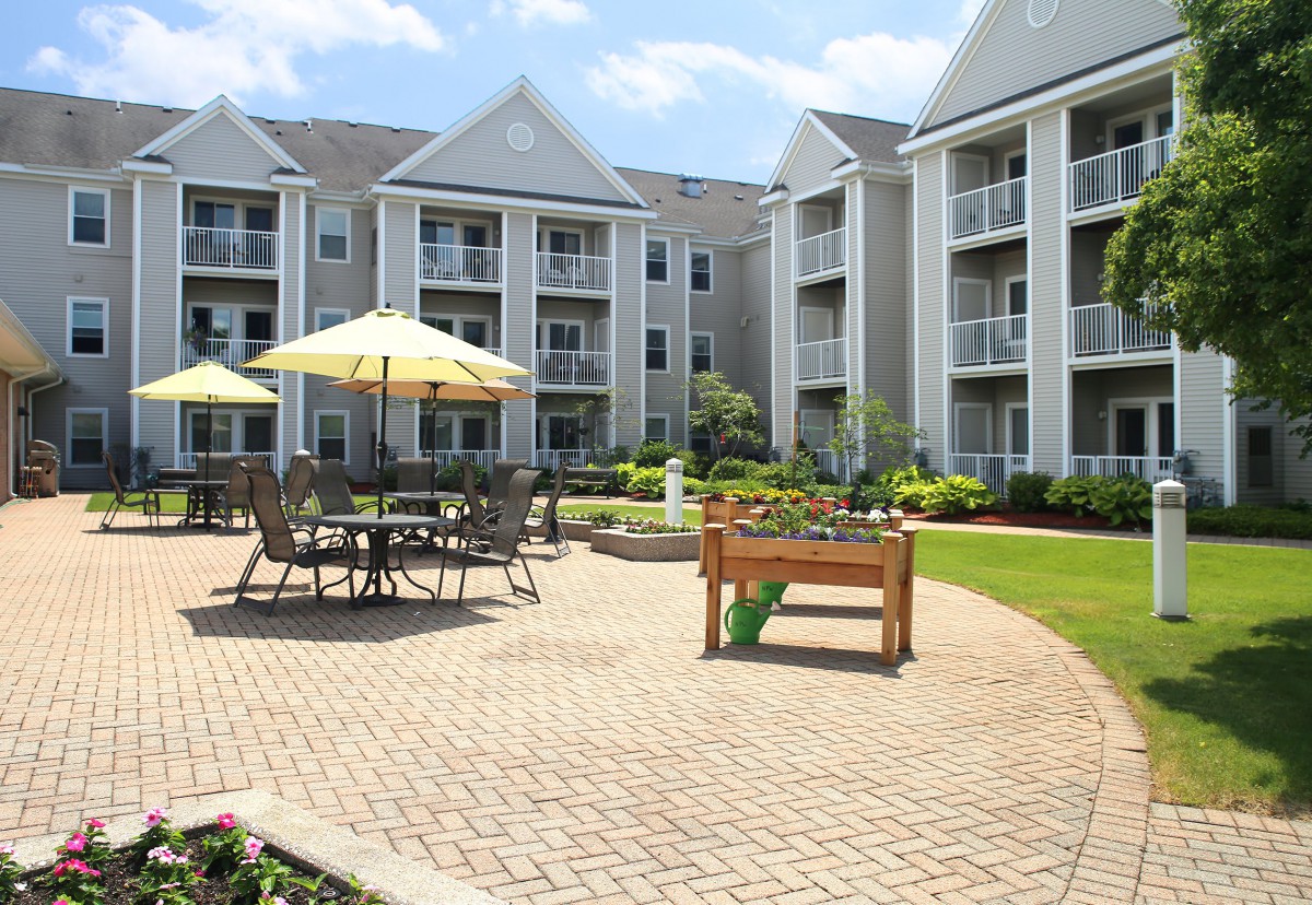 A well-maintained apartment complex courtyard featuring outdoor seating with umbrellas and landscaped surroundings.