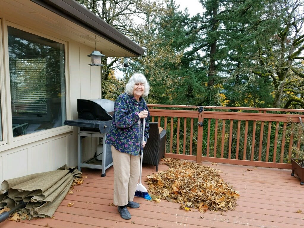 A woman sweeping leaves on a wooden deck in the autumn.