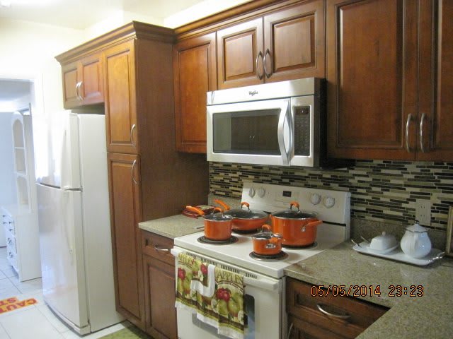 A modern kitchen with wooden cabinets and a variety of appliances, including a microwave and stovetop with orange pots.
