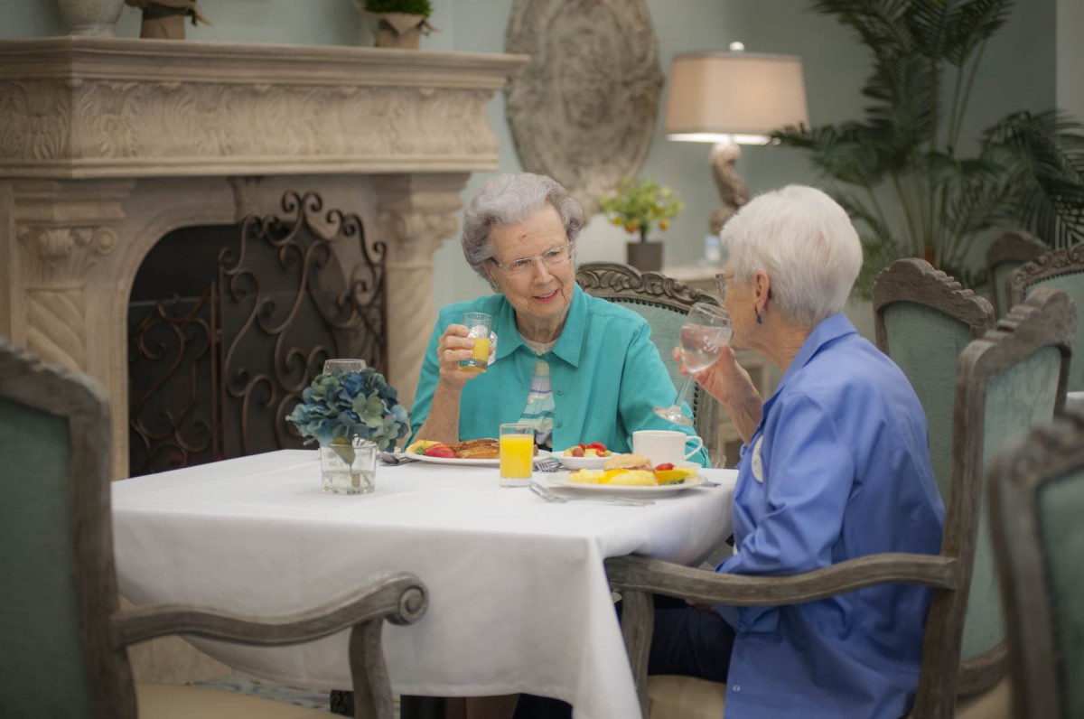 Two elderly women enjoying a meal and conversation at a dining table.