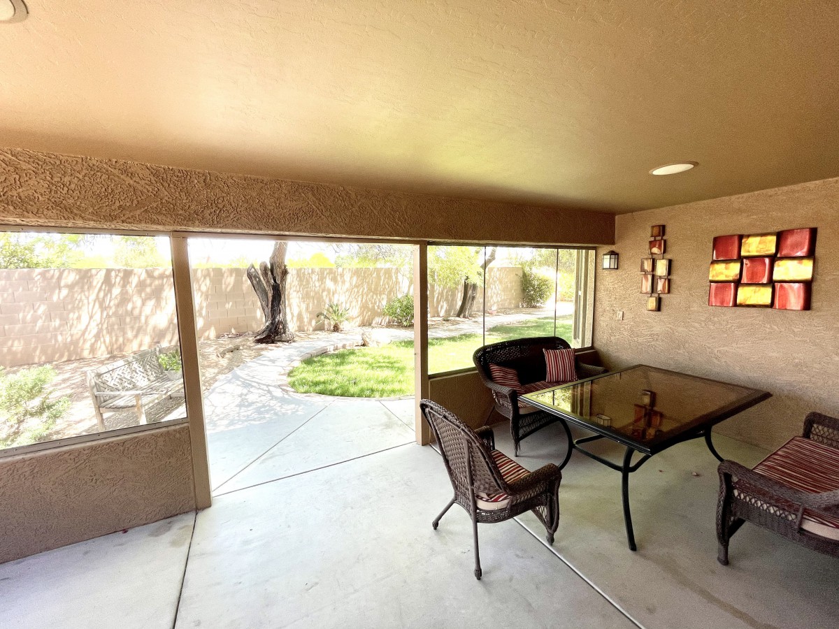 A cozy covered patio with a glass table and chairs overlooking a garden.