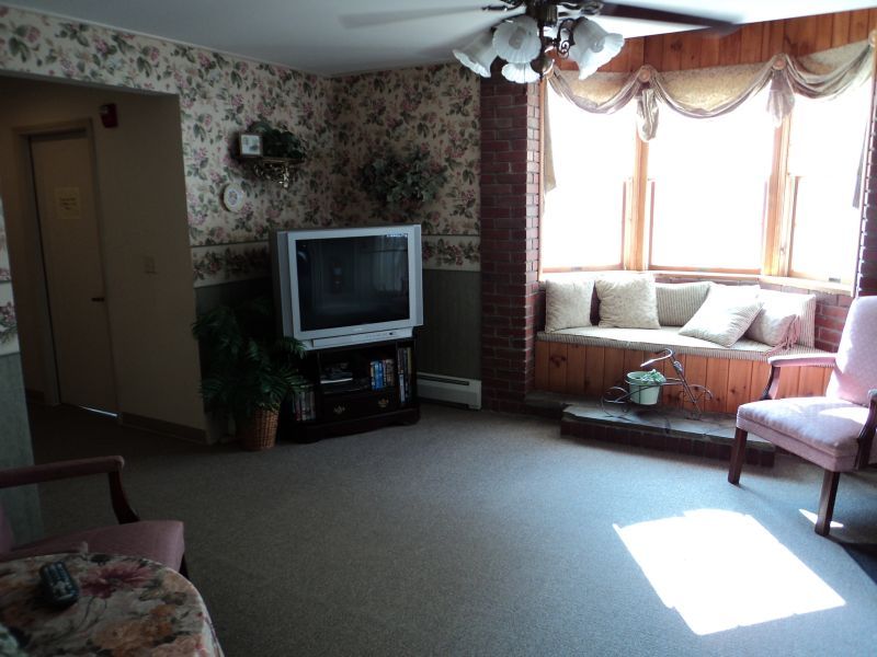 A cozy living room featuring a classic television set, a comfortable window seat, and a ceiling fan.