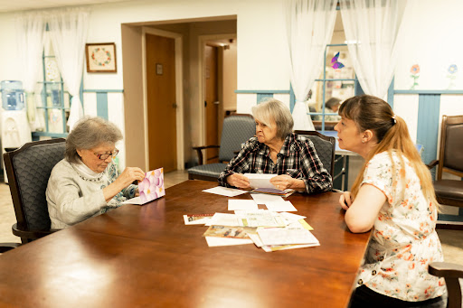 Three women engaged in conversation while looking at photographs at a community center.