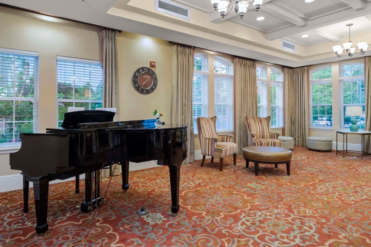 A formal room with a grand piano and elegant seating arrangement, featuring large windows and a decorative chandelier.