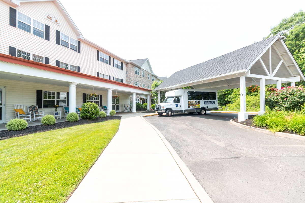 A sunny day view of a building with a driveway and a white van parked under a covered area.