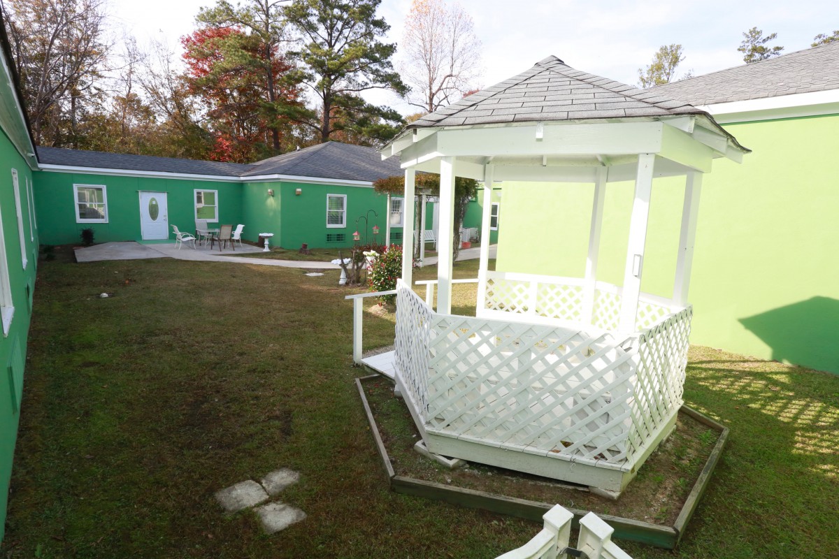 A charming outdoor scene featuring a white gazebo and a green building, surrounded by a well-kept yard.
