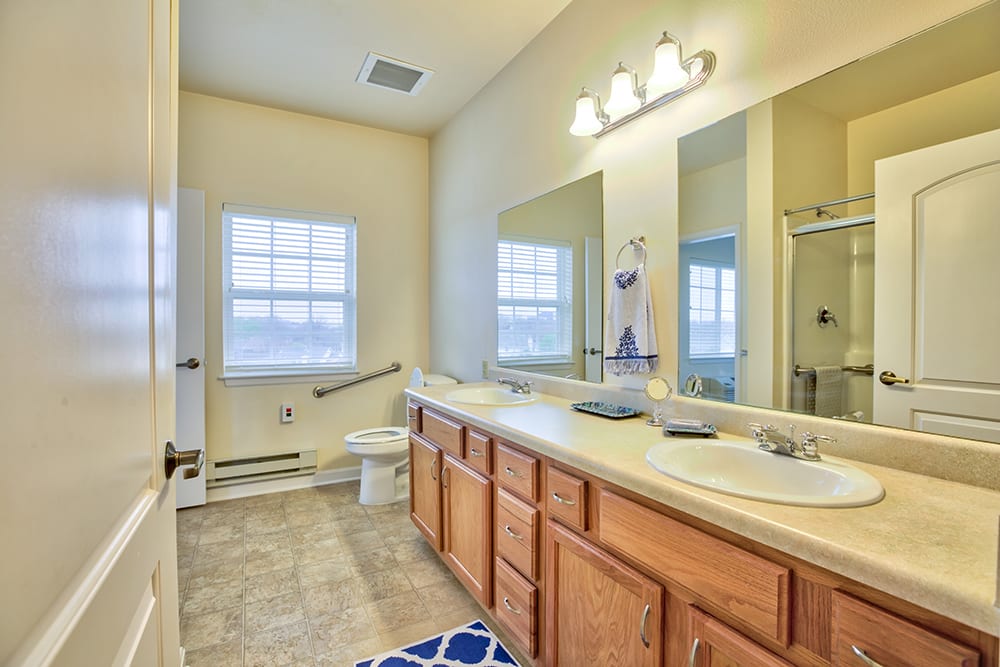 A spacious bathroom featuring double sinks, wooden cabinets, and a large mirror.