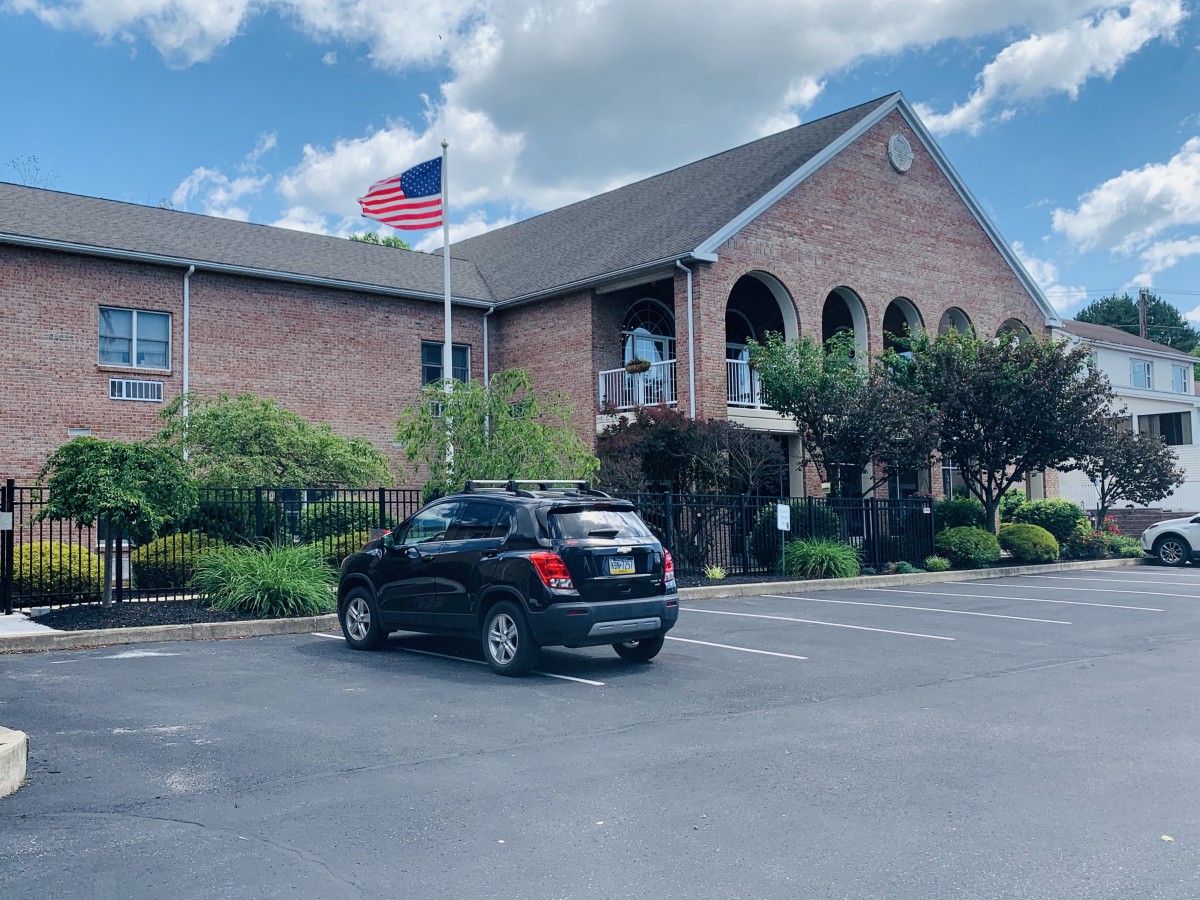 A brick building with an American flag flying outside, surrounded by a parking lot and trees.