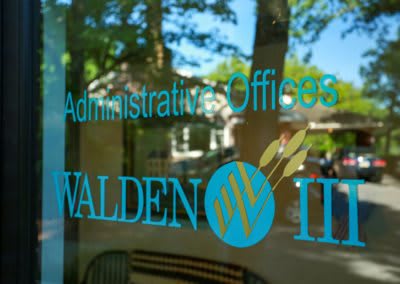 A window with the reflection of trees, featuring signage for an administrative office.