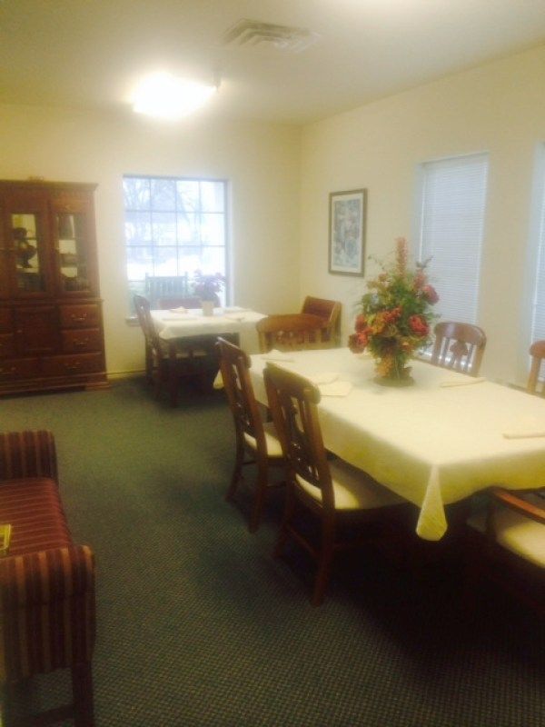 A cozy dining room featuring a table set with chairs, a floral centerpiece, and a cabinet by the window.