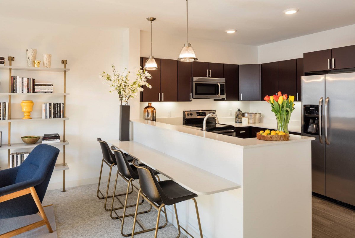 A modern kitchen with sleek design, featuring a countertop with barstools and pendant lighting.