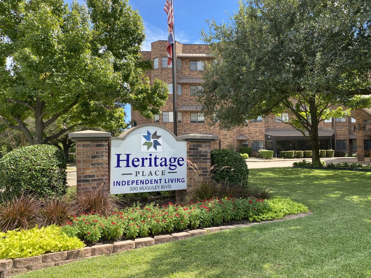 Entrance sign for Heritage Place Retirement Community surrounded by trees and greenery.