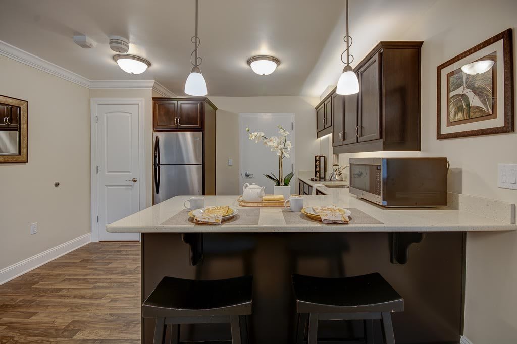 A modern kitchen featuring an island counter with stools, pendant lighting, wood cabinets, and stainless steel appliances.