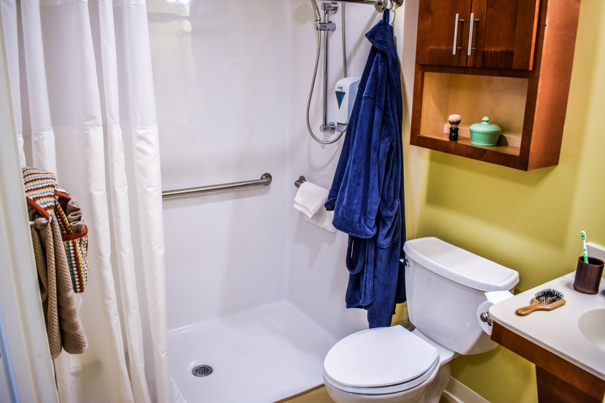 A small bathroom featuring a shower with a grab bar, a toilet, and shelves with bathroom essentials.