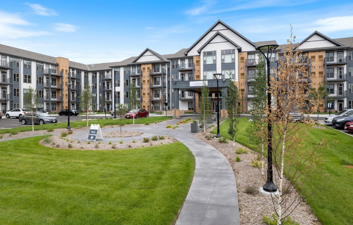 A modern apartment building surrounded by well-maintained landscaping and a winding pathway.