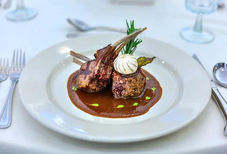 Gourmet lamb chops elegantly plated with rich sauce and garnished with herbs.