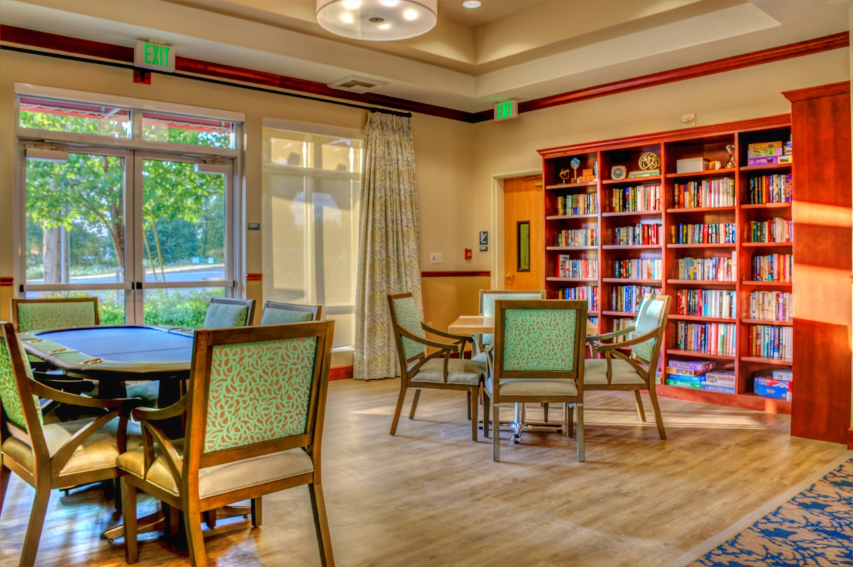 A cozy reading room with bookshelves, tables, and chairs near large windows.