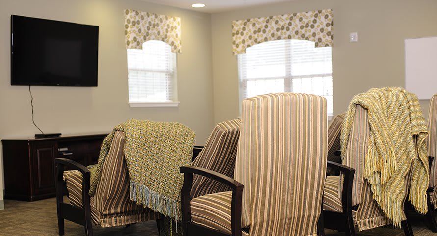 A room with striped upholstered chairs and patterned drapes near windows.