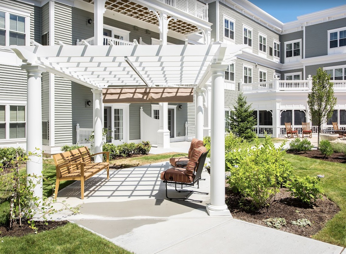 A beautiful patio area with a pergola, benches, and lush landscaping outside a residential building.