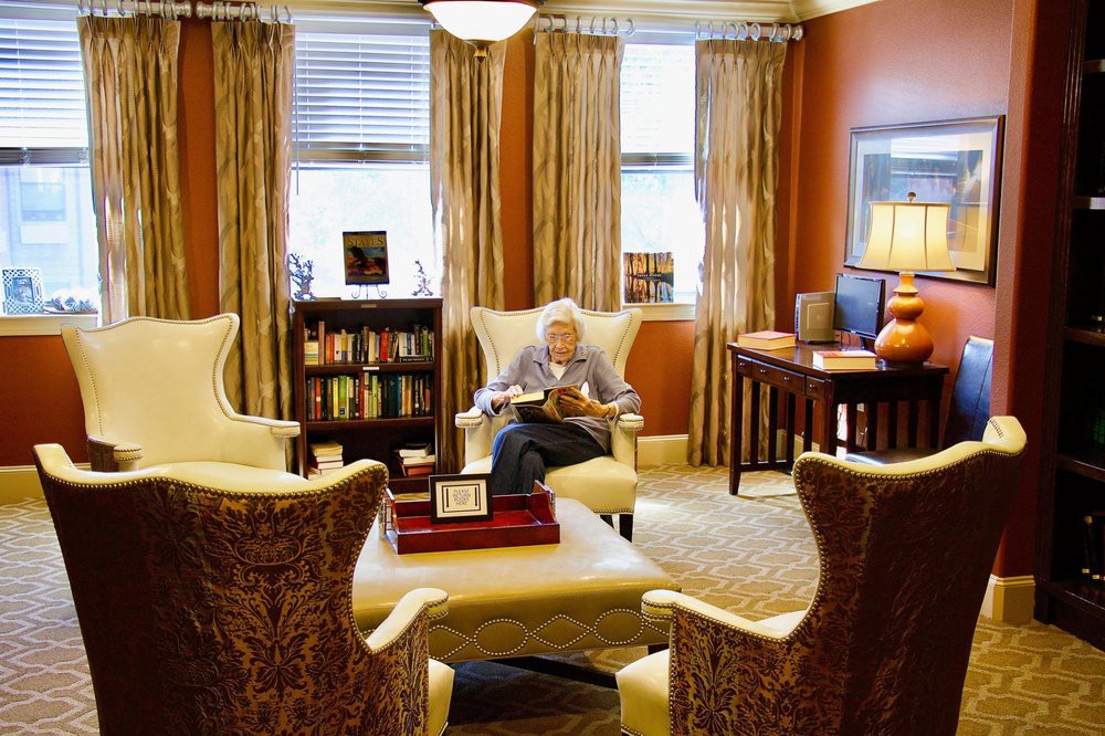 A person reading in a cozy library room with armchairs and bookshelves.