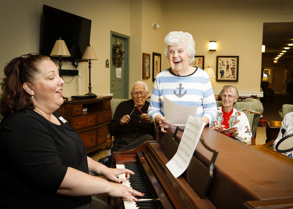 A group of elderly individuals enjoying a singing session with piano accompaniment.