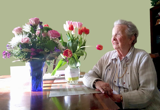 An elderly woman enjoys the beauty of colorful flowers on a sunny day.