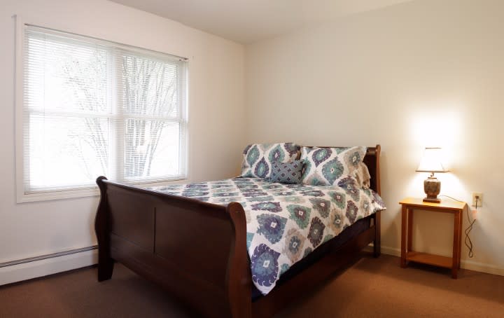 A cozy bedroom with a wooden bed frame and patterned bedding next to a window.