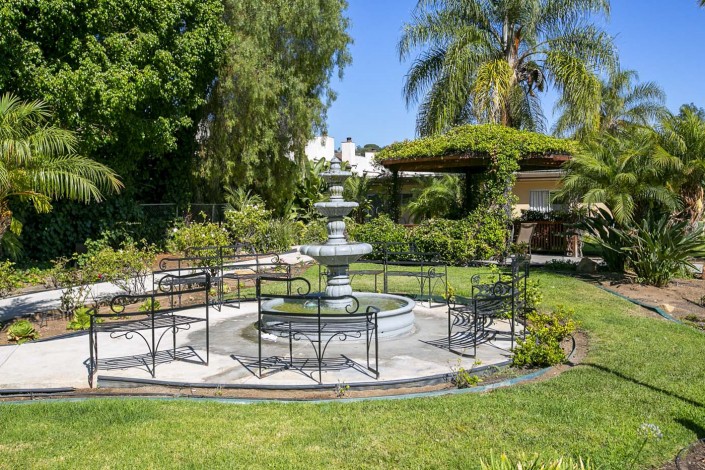 A serene outdoor garden area featuring a central fountain surrounded by chairs and lush greenery.
