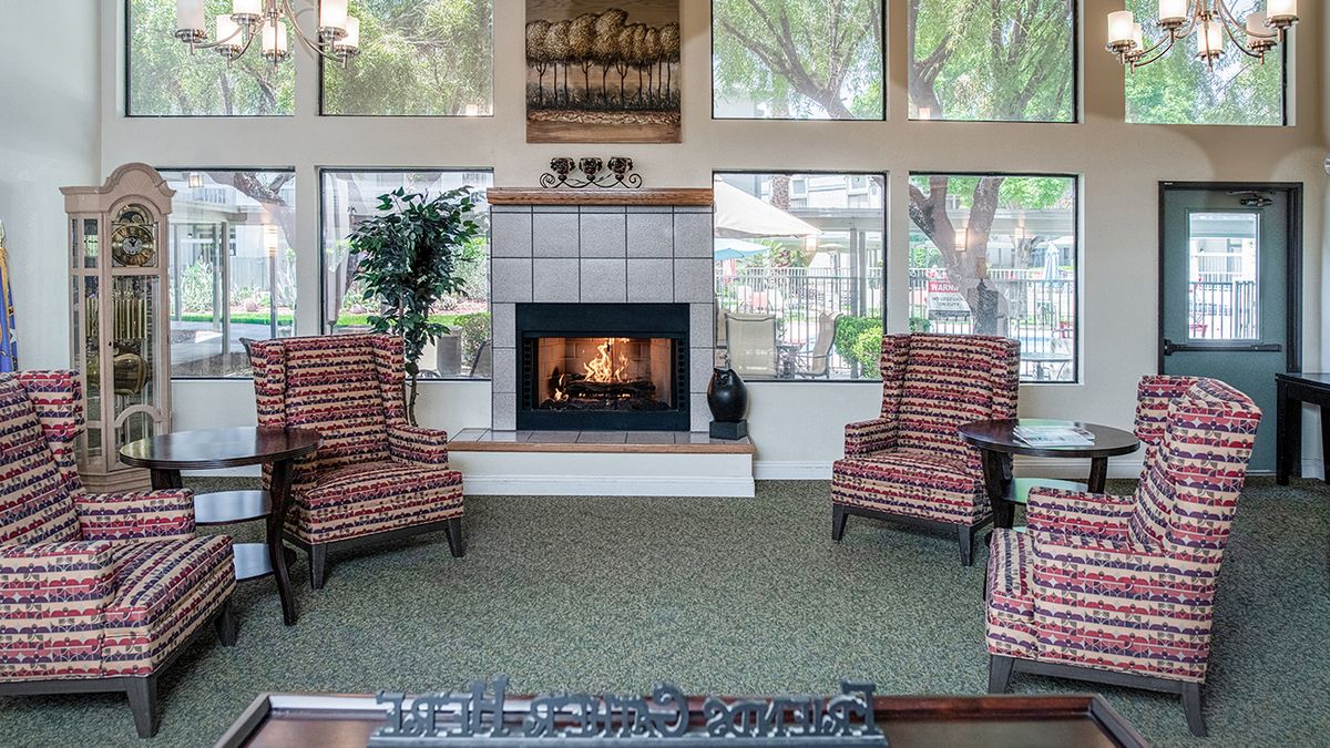 A cozy living room with a fireplace and two armchairs, surrounded by large windows.