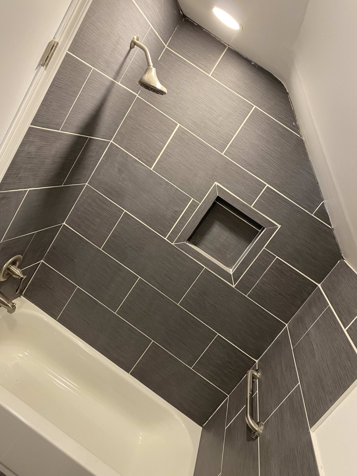 A modern bathroom with gray tiled walls and a built-in wall niche above the bathtub.