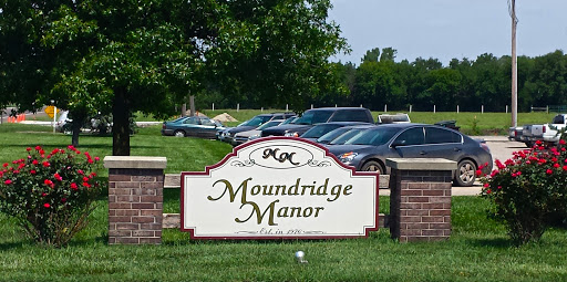 Entrance sign of Moundridge Manor with parked cars in the background.