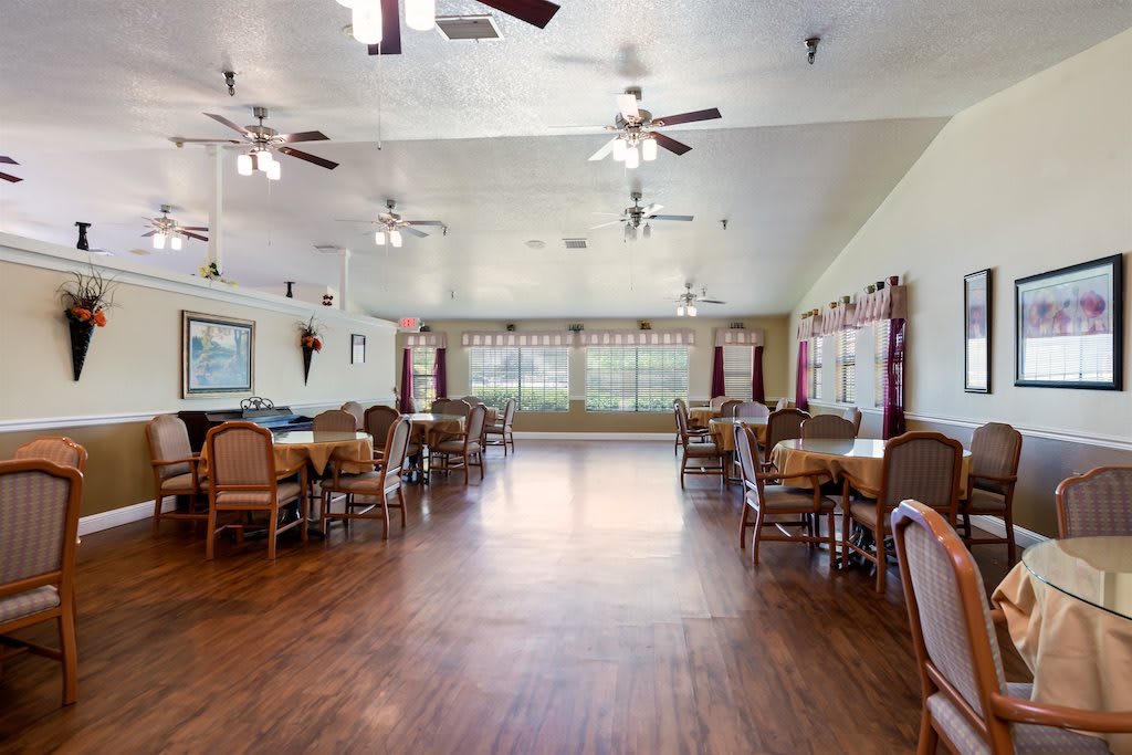 A spacious dining area with wooden floors and multiple ceiling fans, furnished with several tables and chairs.