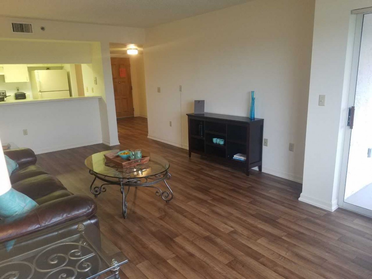 A cozy living room with wood flooring, featuring a coffee table and a shelving unit.