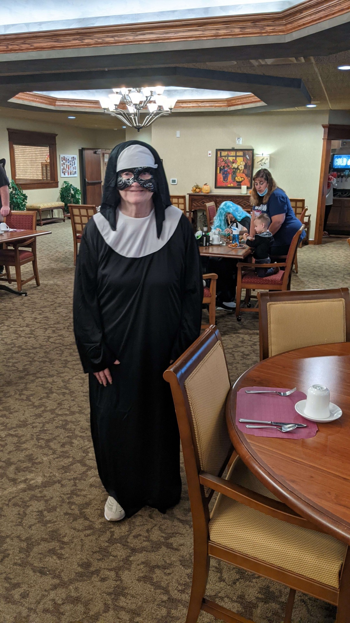 A person dressed in a nun costume stands in a restaurant setting.